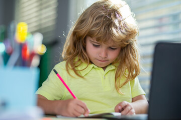 Serious school child writing homework in school class. Portrait of school kid boy siting on table doing homework. Child holding pencil and writing. Boy drawing on white paper at the table.