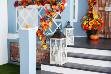 House entrance staircase decorated for autumn holidays, fall flowers and pumpkins. Cozy porch of the house with wooden lanterns in fall time. Halloween design home with yellow fall leaves and lamps	
