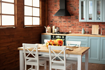Interior design scandinavian kitchen with utensils, dishes, plates. Stylish dining room with wooden table and chairs. Cozy cuisine decorated with fall decor and table setting flowers and pumpkins. 