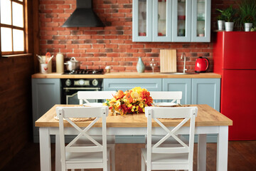 Interior design scandinavian kitchen with utensils, dishes, plates. Stylish dining room with wooden table and chairs. Cozy cuisine decorated with fall decor and table setting flowers and pumpkins.	