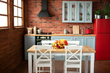 Stylish dining room with wooden table and chairs. Cozy cuisine decorated with fall decor and table setting flowers and pumpkins. Interior design scandinavian kitchen with utensils, dishes, plates. 
