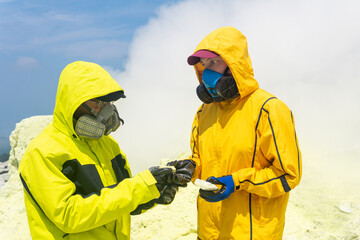 volcano scientists on the slope of the volcano examines samples of minerals against the backdrop of...