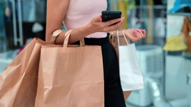 Unrecognizable pretty woman going at store mall showcase with paper shopping bag smartphone closeup