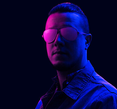 Young Millennial Man Wearing A Denim Jacket And Sunglasses In Neon Pink Studio Light.