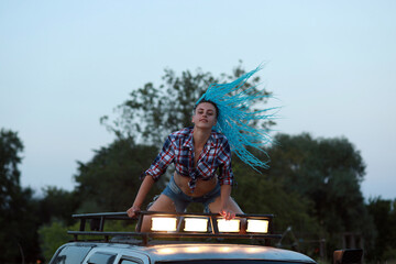 Fototapeta na wymiar Woman with blue hair on a roof of a car