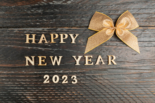 Happy new year festive greeting card. gold ribbon tied in a bow and wooden text happy new year 2023 on festive wooden table.