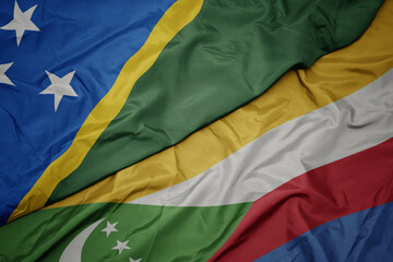 waving colorful flag of comoros and national flag of Solomon Islands .