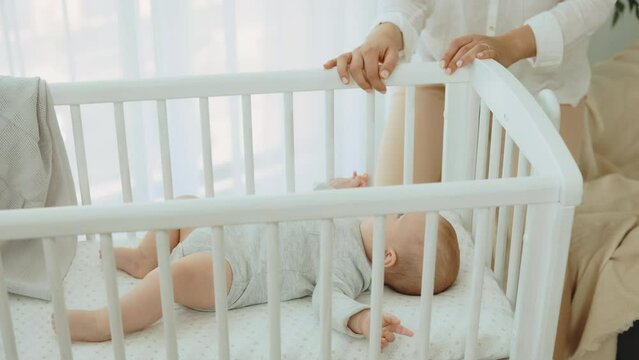 Close view of the woman hands rocking the baby cot with newborn baby inside wearing cute baby bodysuit. Newborn baby concept