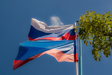 Luhansk People's Republic flag of  flies against a clear blue sky with white clouds. Russian flag