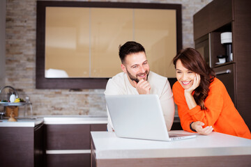 Smiling couple using laptop while standing at the kitchen at home