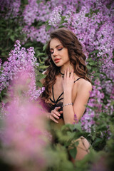 Obraz na płótnie Canvas a beautiful girl with makeup and hair styling in underwear stands in a garden with lilacs on a summer evening