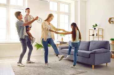 Happy, joyful family having fun at home. Cheerful, carefree mother, father and children spending time in their spacious modern living room, playing games and dancing