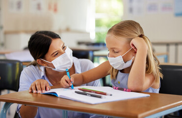 Fototapeta premium Education, covid and learning with face mask on girl doing school work in classroom, teacher helping student while writing in class. Elementary child wearing protection to stop the spread of a virus