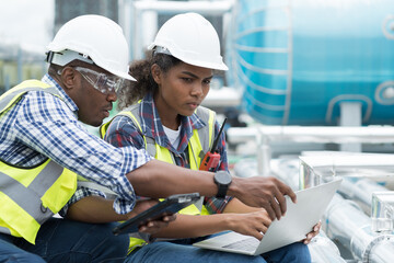Group of African American engineer working in sewer pipes area at construction site. Male engineer and woman engineer discussing for maintenance sewer pipes, water tank on rooftop of building - obrazy, fototapety, plakaty