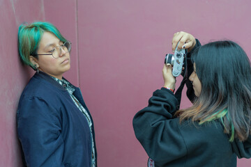 Lesbian woman taking a portrait of her partner with a digital camera in the street