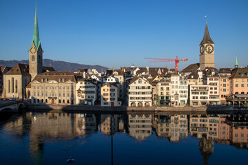 Fototapeta na wymiar Altstadt in Zürich, Blick auf die Kirchen St. Peter und Fraumünster über der Limmat, Spiegelungen im Sonnenlicht am Morgen