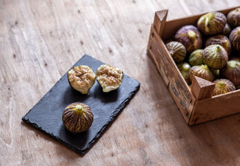 Fresh figs on a black slate plate, next to a wooden box with figs. 