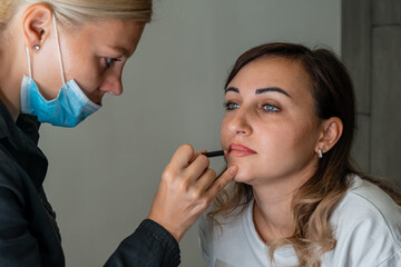 Girl make-up artist works with a client in the salon. Draws the contour of the lips, emphasizing and highlighting them. Job in the beauty industry with beautiful people