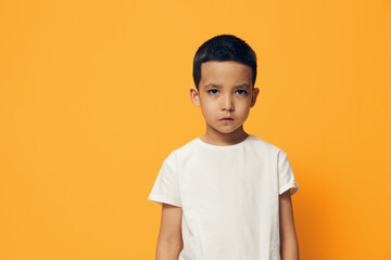 a sad, upset boy, looking angrily at the camera, standing on an orange background in a white cotton T-shirt. Horizontal photo with advertising space