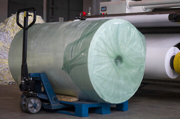 Large jumbo roller of white paper on a wooden pallet in the workshop printing house. Preparation material for cutting machine. Production self-adhesive material for printing houses. Selective focus