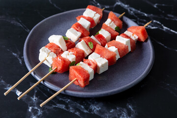 Watermelon and cheese skewers with mint leaves on a black background