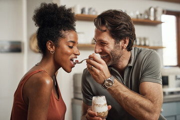 Romantic, happy and interracial couple eating a healthy yogurt together in a cute, sweet and fun...