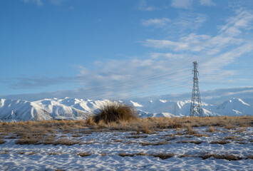 High voltage transmission towers and powerlines with snow-covered Ben Ohau range in the distance,...