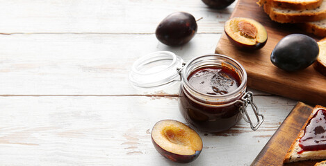 Glass jar with delicious homemade plum jam on wooden background