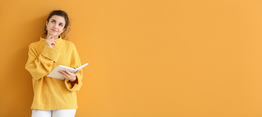 Thoughtful young woman in autumn clothes and with book on orange background with space for text