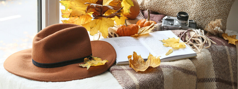Autumn composition with book, felt hat and photo camera on windowsill
