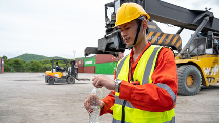 Foreman or worker is drinking a bottle of water after finishing work and relaxing on the old truck at cargo container port