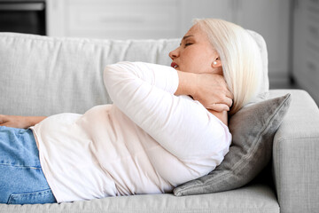 Mature woman suffering from neck pain on sofa at home