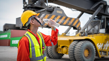 Foreman or worker is drinking a bottle of water after finishing work and relaxing on the old truck at cargo container port