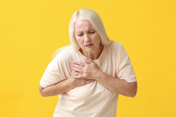Mature woman suffering from breast pain on yellow background