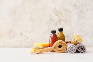 Different cleaning supplies, bottles and towels on white wooden table against grunge background