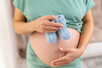 Maternity big belly. Happy pregnant lady holding small shoes. - obrazy, fototapety, plakaty