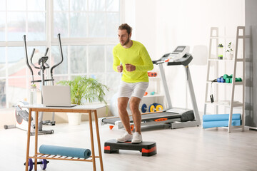 Sporty young man using laptop for online training in gym