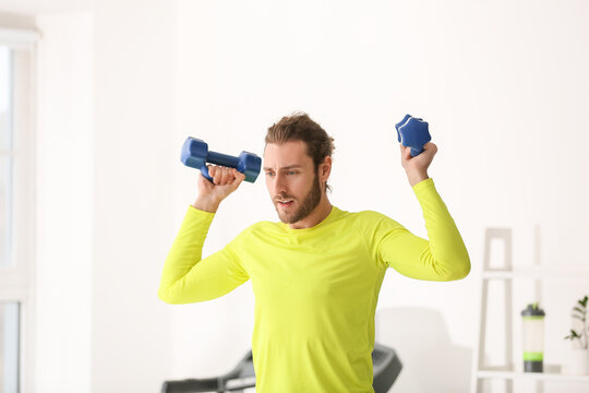 Sporty Young Man Using Dumbbells In Gym