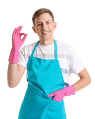 Young man in rubber gloves and apron showing OK on white background