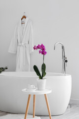 Orchid flower and cup on table near bathtub