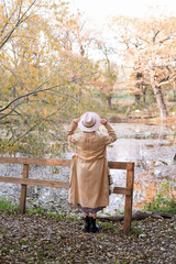 rear view of beautiful woman in beige coat and hat by the lake in autumn park in fall
