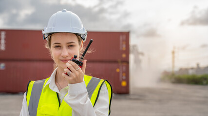 Woman foreman smile using walkie talkie in front of Cargo forklift in warehouse , Manager in white helmet Safety Supervisor in Container Custom Terminal port concept import export
