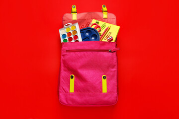 Pink backpack with school stationery on red background