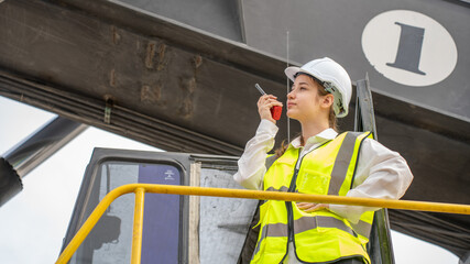 Female Foreman stay on lifting forklift container cargo forklift using walkie talkie for communication and control forklift concept service transportation logistic. Safety supervisor in white helmet