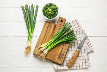 Composition with fresh green onion and knife on light wooden background