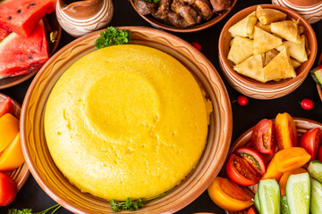 Homemade Romanian Food with polenta, meat, cheese and vegetables. Delicious corn porridge in clay dishes. Mamaliga or polenta, a traditional dish in Moldova, Hungary and Ukrainian cuisine.
