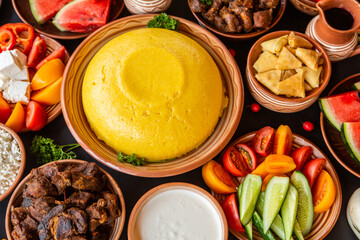 Homemade Romanian Food with polenta, meat, cheese and vegetables. Delicious corn porridge in clay dishes. Mamaliga or polenta, a traditional dish in Moldova, Hungary and Ukrainian cuisine.
