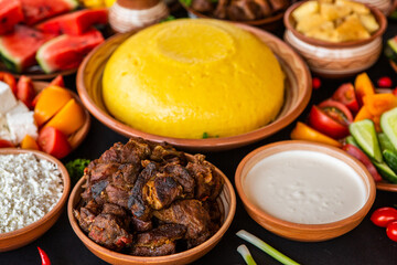 Homemade Romanian Food with polenta, meat, cheese and vegetables. Delicious corn porridge in clay dishes. Mamaliga or polenta, a traditional dish in Moldova, Hungary and Ukrainian cuisine.
