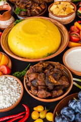 Homemade Romanian Food with polenta, meat, cheese and vegetables. Delicious corn porridge in clay dishes. Mamaliga or polenta, a traditional dish in Moldova, Hungary and Ukrainian cuisine.

