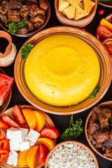 Homemade Romanian Food with polenta, meat, cheese and vegetables. Delicious corn porridge in clay dishes. Mamaliga or polenta, a traditional dish in Moldova, Hungary and Ukrainian cuisine.
